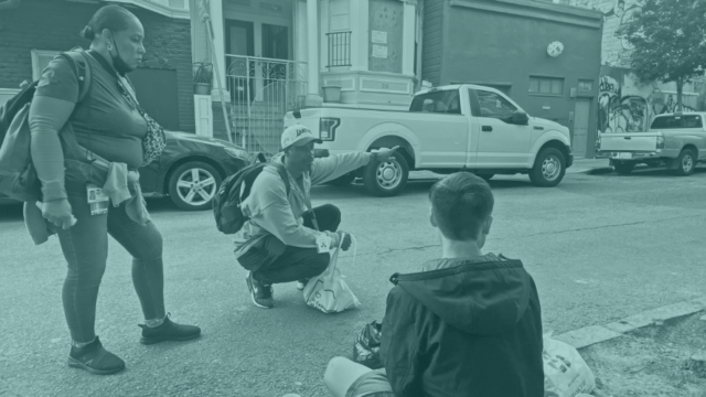 Two public health workers talking with a young man who is sitting on the sidewalk